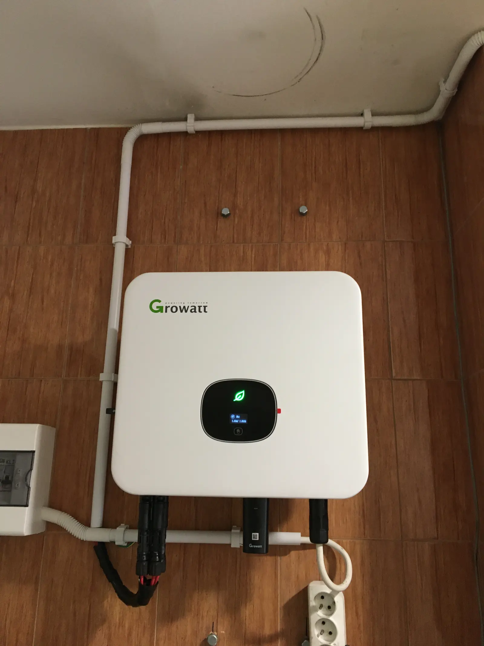 Falownik Growatt na ścianie wyłożonej płytkami, z rurkami instalacyjnymi