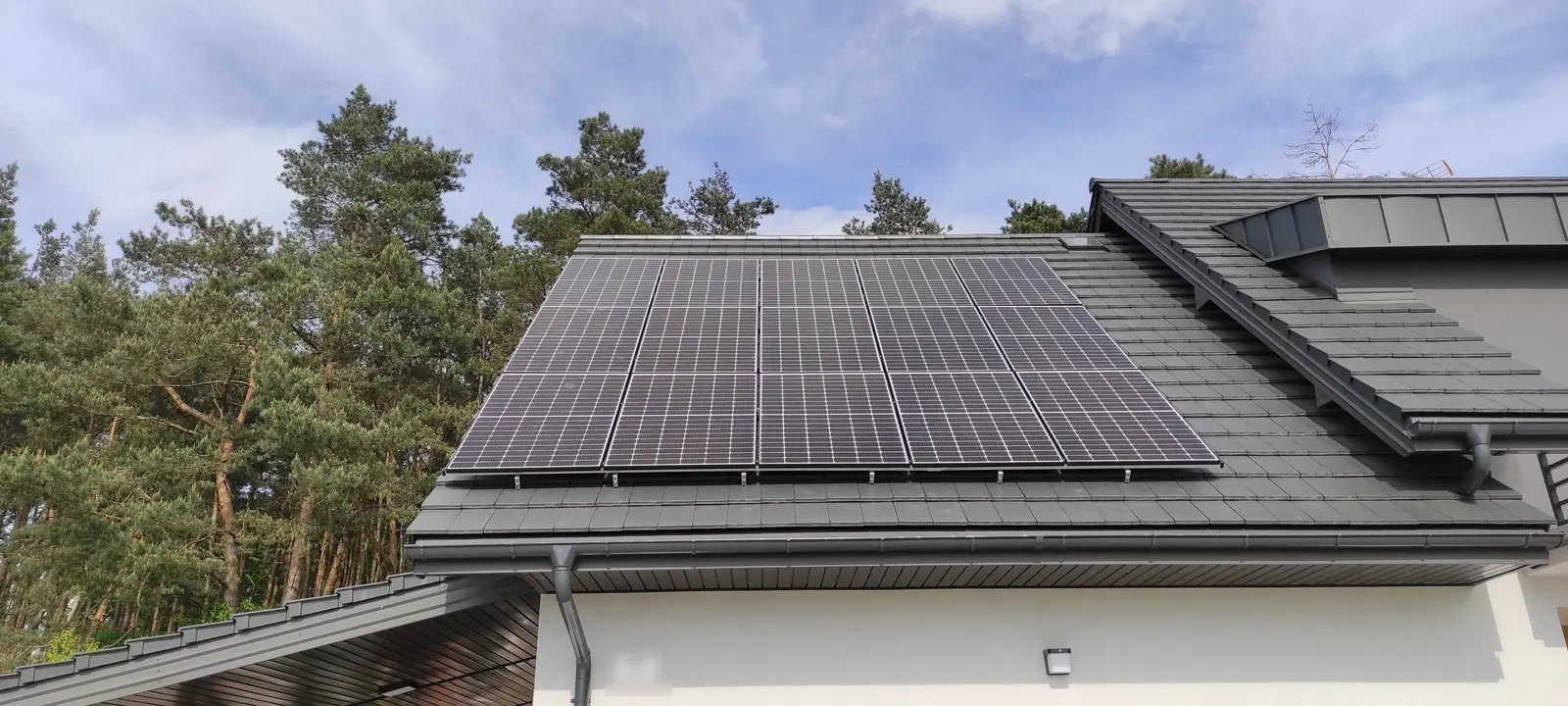 Instalacja fotowoltaiczna na dachu domu otoczonego sosnowym lasem