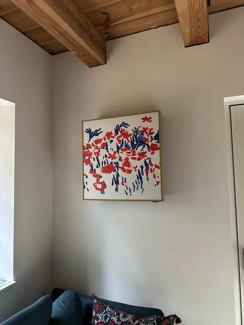 Klimatyzator LG Artcool Gallery w formie obrazu, z kwiatową grafiką w jasnej ramie, na ścianie pokoju z drewnianym stropem belkowym