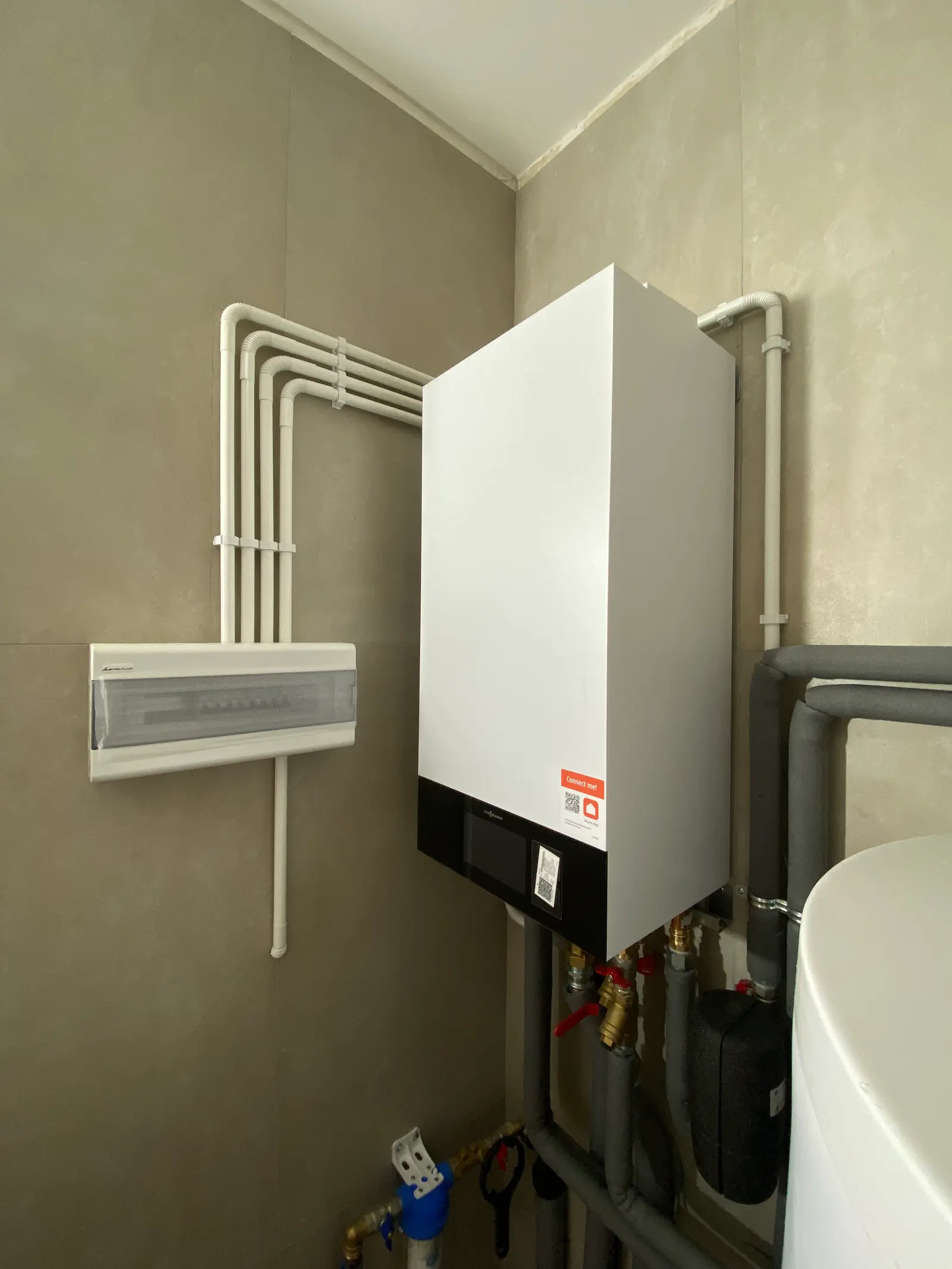 Wisząca biała jednostka grzewcza obok rozdzielnicy elektrycznej w pomieszczeniu technicznym